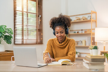Distance Education. Portrait of smiling woman african american sitting at desk, using laptop and writing in notebook, taking notes, watching tutorial, lecture or webinar, studying online at home
