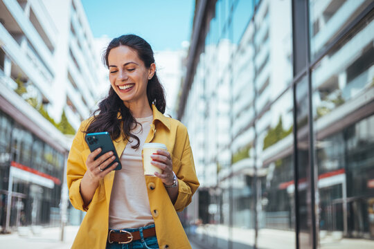 Woman texting and drinking coffee outdoors. Artificial intelligence and communication network concept.Beautiful young woman using a smartphone.