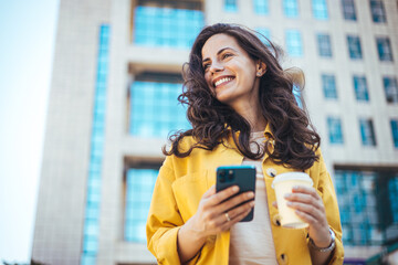 Beautiful young woman is using an app in her smartphone device to send a text message near business...