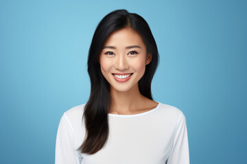 Pretty Asian woman with dark hair, wearing a white shirt and jumper, smiles pleasantly at the camera with a toothy smile. Isolated over a blue background. - Powered by Adobe