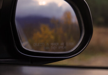 The car side mirror with the inscription reflects the autumn forest