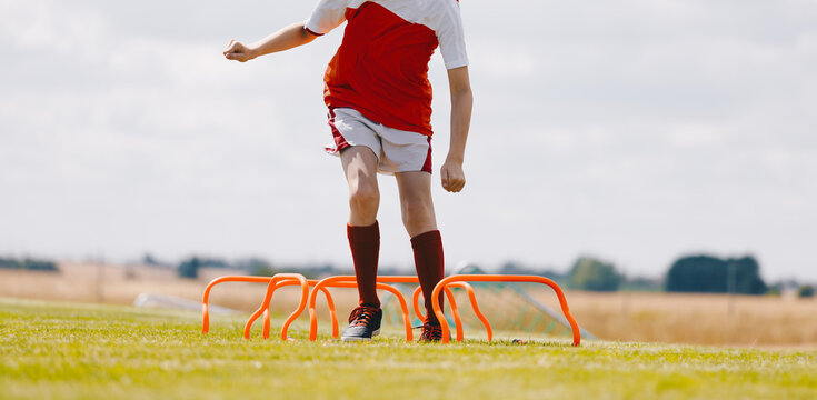 Teenage boy jumping over hurdles. Young soccer athlete practicing strength and agility skills at soccer school academy. Soccer coach coaching a young player