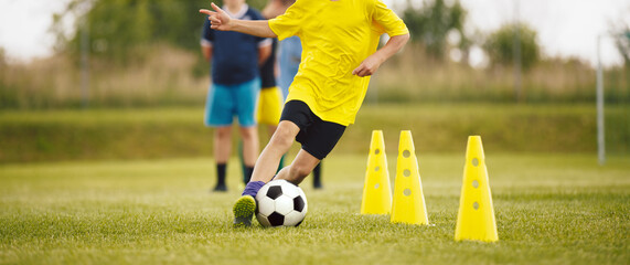 Football Drills: The Slalom Drill. Youth soccer practice drills. Young football players training on pitch. Soccer slalom cone drill. Boy in yellow soccer jersey shirt running with ball between cones