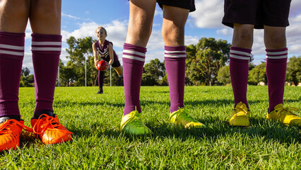 three pairs of legs in football boots and long socks standing on grassed oval