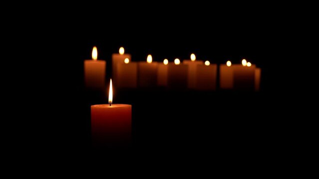 one lighted candle in front of a lot of blurred candles isolated on black background, texture template overlay for contemplative festive mood