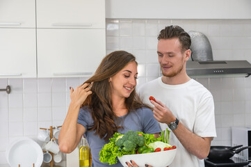 Caucasian young couple in white kitchen cooking making preparing healthy food holding a bowl of mix vegetable.