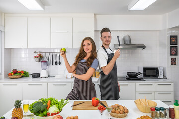 Caucasian young couple in white kitchen cooking making preparing healthy food with vegetables wearing aprons.