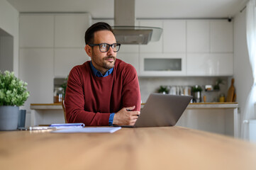 Young businessman thinking about business project and looking away with laptop on desk at home