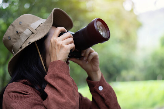 Asian female tourist backpacking in hat taking pictures with camera and going for a tropical forest