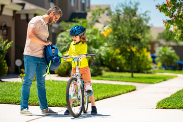 Fototapeta premium Sporty family father and son riding bike on a park. Child in safety helmet riding bike on summer day. Father teaching son riding on bike. Child son in bike helmet on bicycle. Fatherhood, Fathers day.