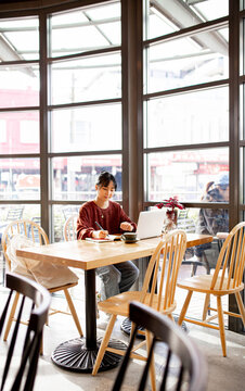 Asian small business owner working remotely on her laptop at a cafe