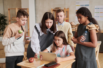 Diverse group of school children using digital tablet in classroom during break