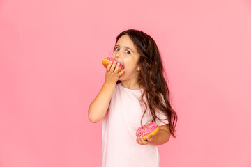 Portrait of a happy little smiling girl with curly hair and two appetizing donuts in her hands on a...
