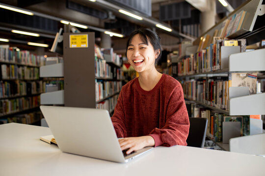 Young adult asian woman at the library studying and using her laptop