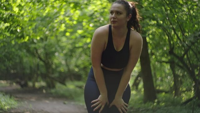 A plus-size woman with an average weight who has trouble breathing while jogging. Energy-consuming training in nature, diet and running and fitness. High quality 4k footage