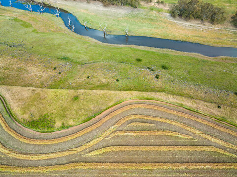 Aerial view of dried canola raked into lines on rural farmland alongside a river