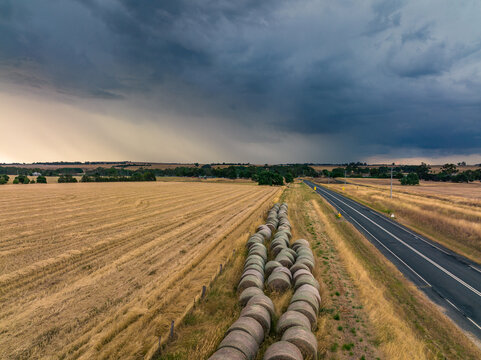 Aerial view of hay bales beside a dry paddock under rain falling from a dark stormy sky