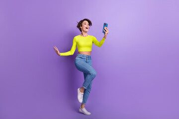 Fototapeta na wymiar Full length portrait of astonished positive person hold smart phone empty space ad isolated on purple color background