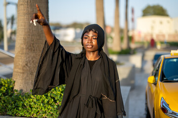 Young beautiful African woman in Abaya hitching a taxi on the street.
