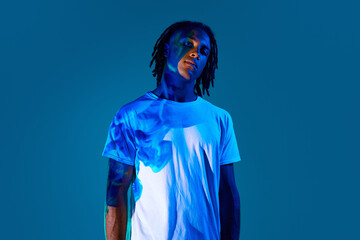 Creative portrait of african young man with dread with neon light reflection on body standing...