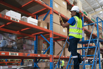 Warehouse worker standing on ladder checking inventory on shelf. Blue collar worker in safety...