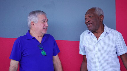 Two Brazilian diverse seniors standing in street conversing and exchanging stories while laughing and smiling, candid authentic elderly interaction in South America