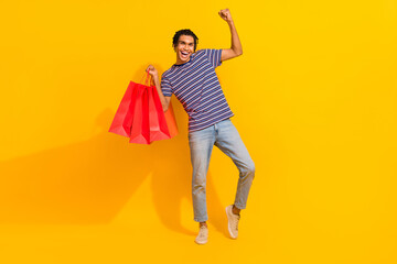Full size photo of delighted cheerful person hold boutique bags raise fist isolated on yellow color...