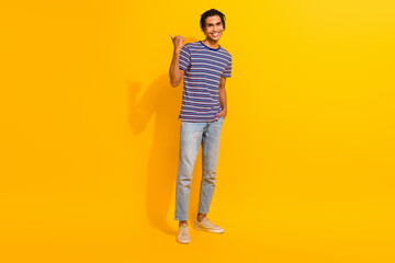 Fototapeta na wymiar Full size photo of satisfied man dressed striped t-shirt directing at promo empty space arm in pocket isolated on yellow color background