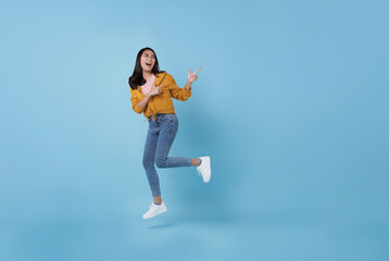 Cheerful positive Asian girl jumping in the air with pointing finger to copy space with smile face and happy isolated on blue background.