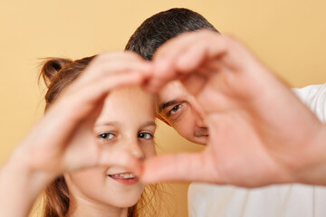 Naklejka premium Smiling brwon haired little girl standing with her father and making heart shape with hands together in fron of their faces expressing love family realtionship.