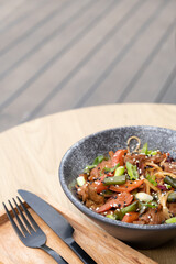 A bowl of udon noodles, veal and fried vegetables angle view on wooden table