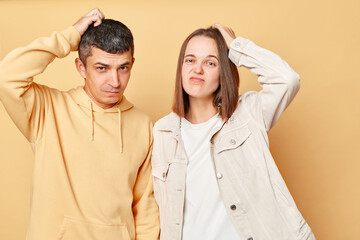 Confused puzzled young man and woman couple standing together isolated over beige background...