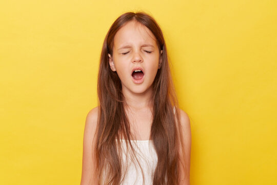 Harmful little girl with ponytails standing isolated over yellow background screming with closed eyes expressing negative emotions.