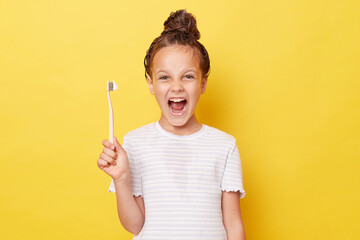 Excited little girl with wet hair wearing casual white T-shirt standing isolated over yellow...
