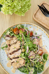 A plate with veal meat on greens with vegetables and olives under nut sauce on a wooden table top view
