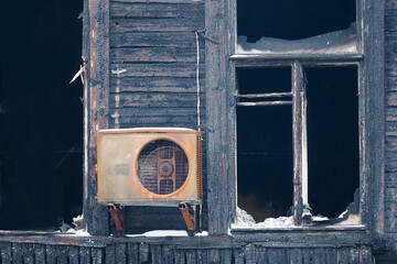 A wooden building after a fire, empty black windows, a burned-out air conditioner