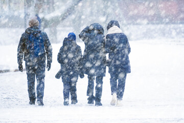 Family walks down the street in winter in a strong snowstorm, winter snowstorm, bad weather