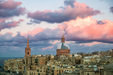 City view and skyline of Valletta at sunset. Historical buildings against blue sky and clouds colored by the sun
