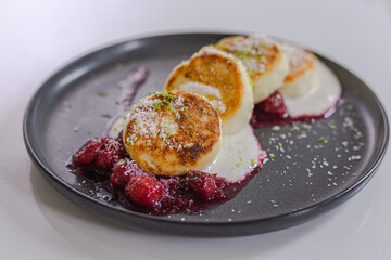 Cottage cheese pancakes, syrniki with fresh berries for breakfast on table on a dark plain plate
