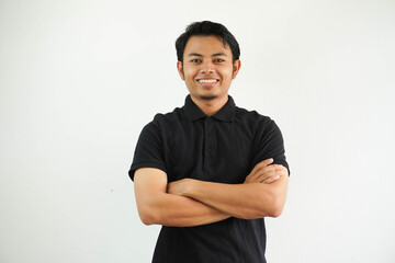 young asian man smiling happy at the camera with arms crossed wearing black polo t shirt isolated...