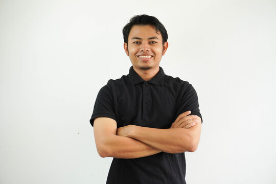 young asian man smiling happy at the camera with arms crossed wearing black polo t shirt isolated on white background
