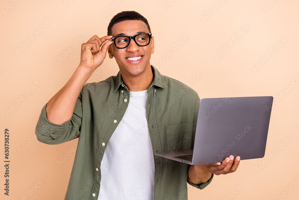 Poster portrait of minded handsome guy arm touch glasses hold netbook look empty space isolated on beige co
