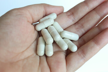 Asian female hand holding white drug capsule. Isolated on white background