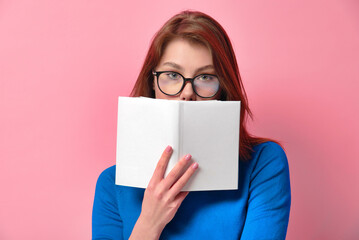 Portrait of a young charming girl with beautiful green eyes in glasses holding a book with a blank...