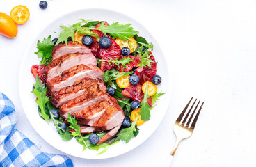 Gourmet salad with grilled duck breast and red orange, kumquat, blueberry, swiss chard, lettuce and arugula on white table background, top view