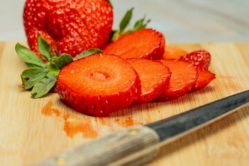 Fresh red strawberries and a knife on a wooden cutting board.