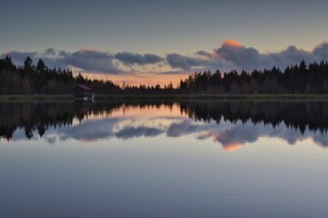 Tranquil landscape of a lake surrounded by lush landscape, with the sun setting in the background