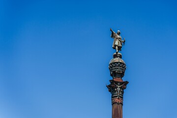 Fototapeta na wymiar Monument and clock tower stand tall against a bright blue sky: Columbus monument in Barcelona