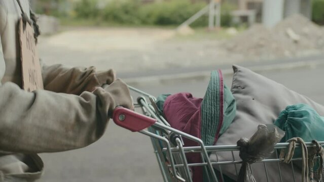 Cropped shot of man walking along road with things in shopping cart in unknown direction