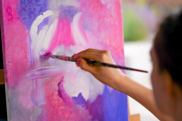 Close-up of a girl artist with a brush applying oil paint to a painting standing on an easel in a studio for painting 